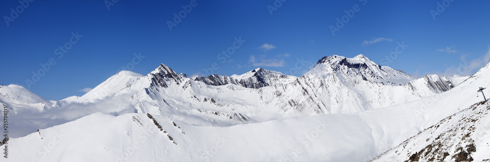 Panorama of mountains with snowy off-piste slope and blue sunlit sky at winter