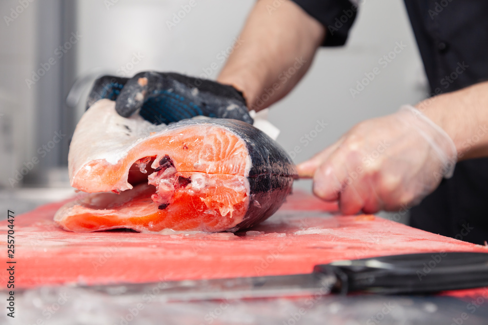 Closeup whole fresh salmon fish preparing fillet with knife on red cutting board in professional kitchen of restaurant. Concept Japanese food, sushi, sashimi, semi finished product, norwegian soup