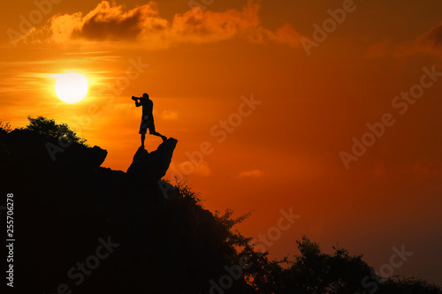 Silhouette of photographer on top of mountain at sunset red sky