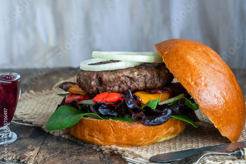 Canvas Print Venison burger in brioche bun with peppery leaf salad, onion, roast peppers and