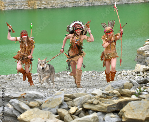 A group of three young girls get dress as native American Indians. They attack with their grey wolf by their side. Behind them a green lake in the middle of a stone quarry.