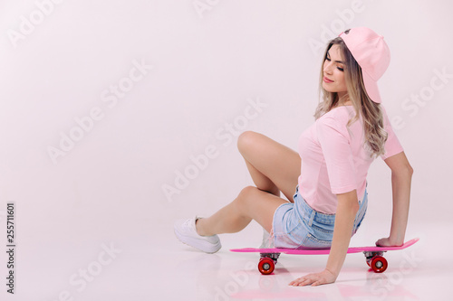 beautiful woman in pink t-shirt and cap sitting on pink skateboard