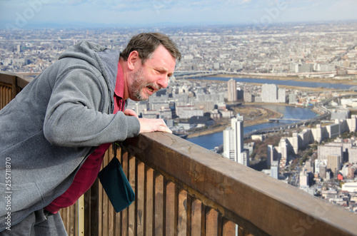 Mature man suffers from acrophobia. He is scared on the viewing platform above a megalopolis. photo