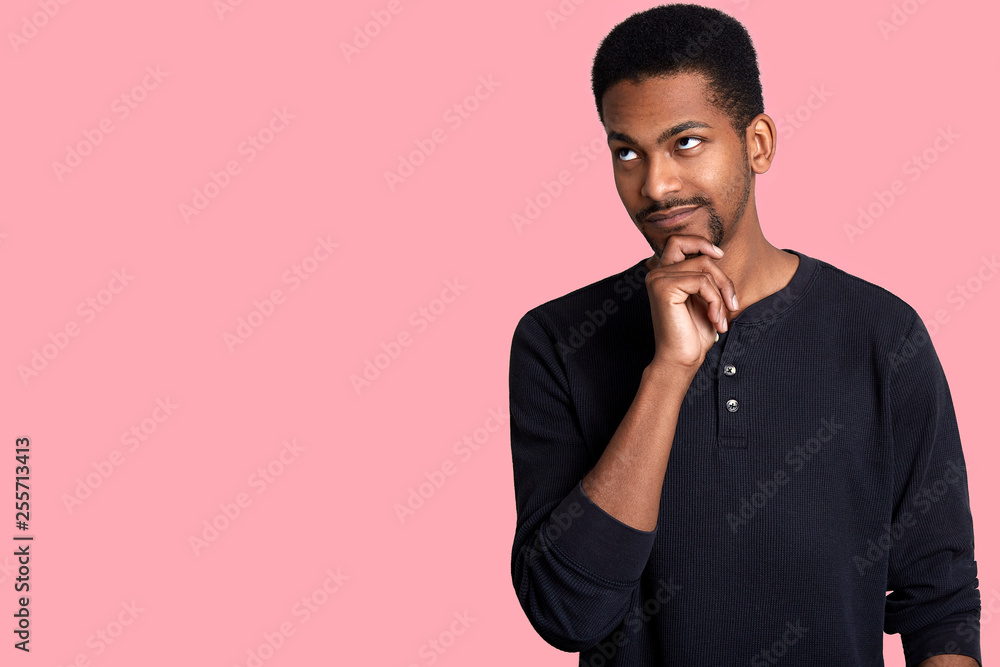 Closeup portrait of attractive thoughtful African guy. Young handsome man looks aside, keeps hand on chin and thinks about his dream, isolated on rose background. Copy space for your advertisment. Closeup portrait of attractive thoughtful African guy. Young handsome man looks aside, keeps hand on chin and thinks about his dream, isolated on rose background. Copy space for your advertisment.
