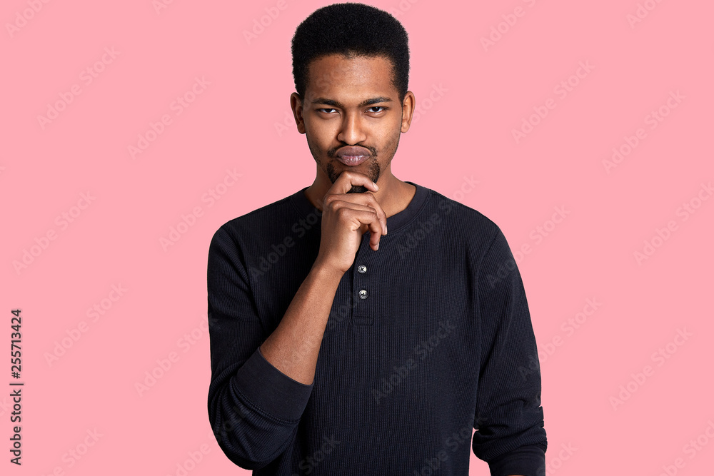 Single handsome fit black man, keeps hand on chin. Guy has thoughtful fecial expressions, has interesting idea and thinks how to bring it to life. Handsome male isolated over pink background. Single handsome fit black man, keeps hand on chin. Guy has thoughtful fecial expressions, has interesting idea and thinks how to bring it to life. Handsome male isolated over pink background.