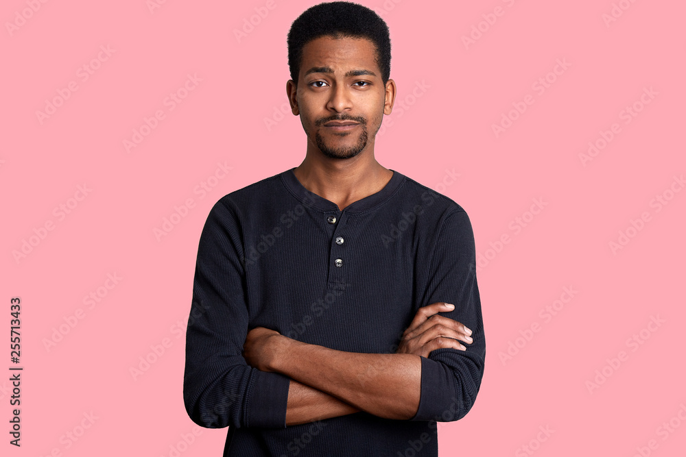 Young dark skinned man with calm expression, short hairstyle and beard, dresses casual shirt and keeps hands crossed. Black male looks at camera, poses isolated over pink background. People concept. Young dark skinned man with calm expression, short hairstyle and beard, dresses casual shirt and keeps hands crossed. Black male looks at camera, poses isolated over pink background. People concept.