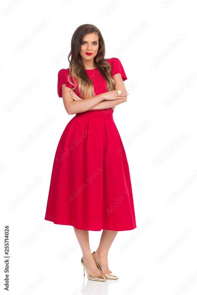 Beautiful Woman In Elegant Red Dress And Gold High Heels Is Standing With Arms Crossed Beautiful Woman In Elegant Red Dress And Gold High Heels Is Standing With Arms Crossed