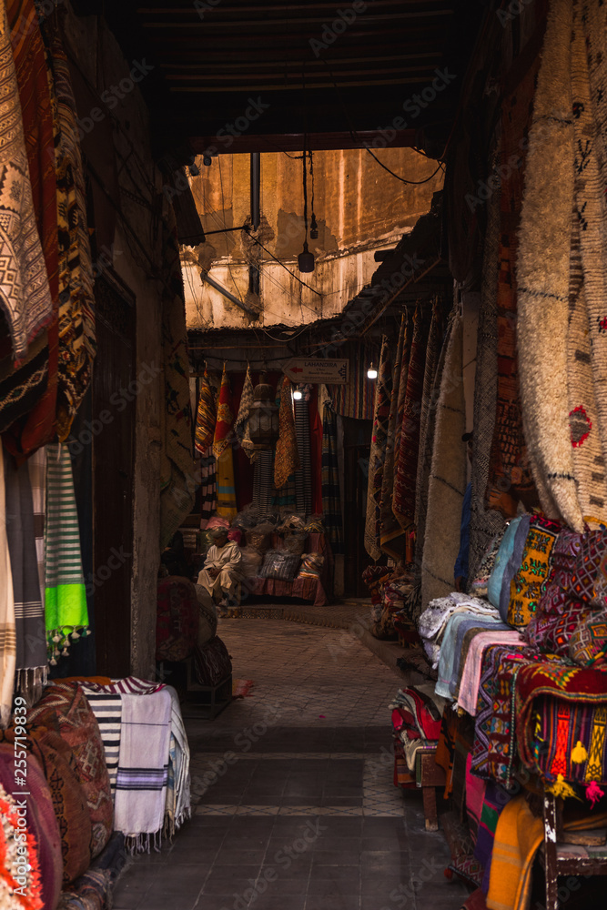 Typical Moroccan alley in the souks of the Medina of Marrakesh with a variety of scarfs and other weaving products (Marrakesh, Morocco, Africa)