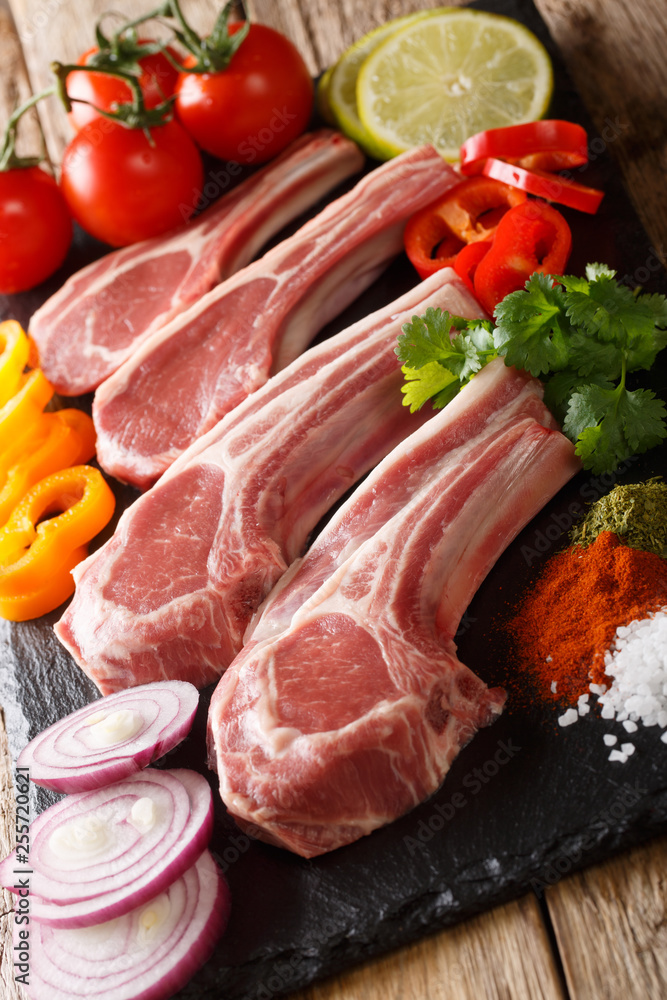 Fresh raw lamb chops on the bone with vegetable ingredients close-up. vertical