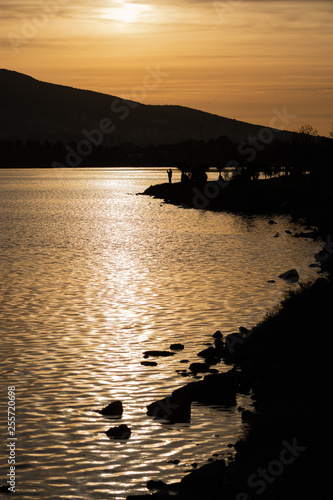 Orange sky at sunset. Sun rays reflected in the water. Mountain and fisherman...