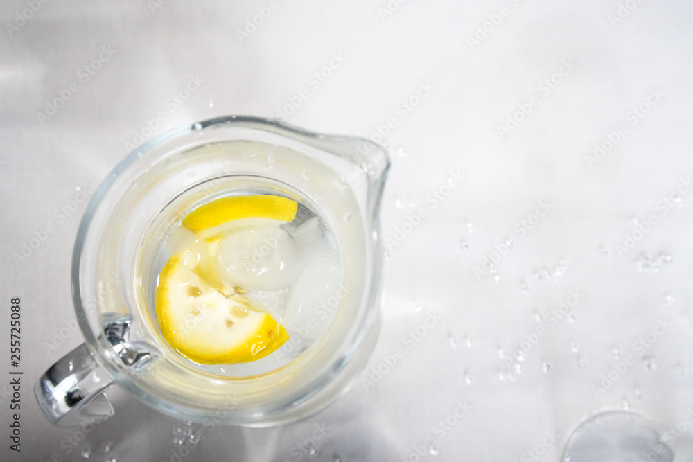 Clear glass jug with water, ice and lemon slices on white background with glitter. Overhead view Clear glass jug with water, ice and lemon slices on white background with glitter. Overhead view