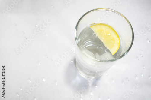 Clear glass with water, ice and lemon slices on white background with glitter