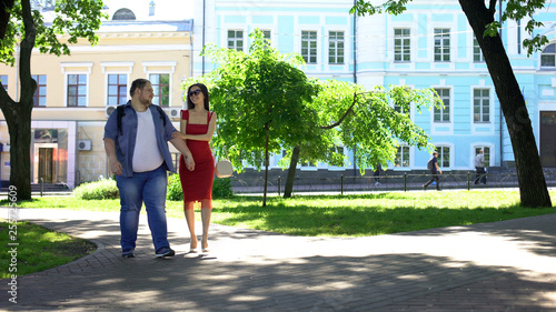 Beautiful woman and fat man holding hands walking in park, dream, leisure time