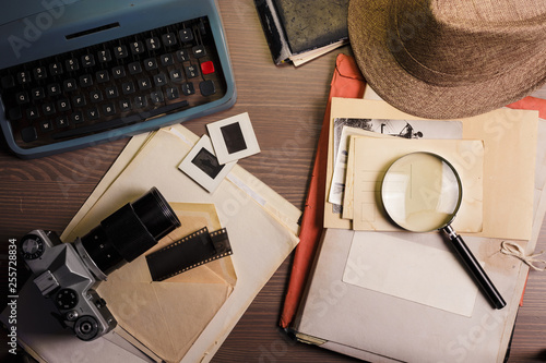 Investigator desk with confidential documents, camera, magnifying glass, vintage typewriter and hat. Secret documents investigation concept.