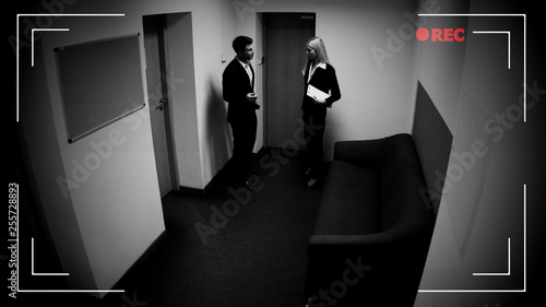Male and female colleagues talking office corridor, CCTV camera effect, footage photo