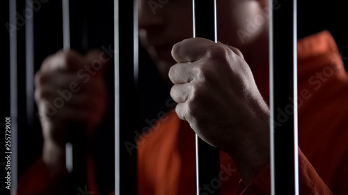 Desperate criminal holding jail bars feeling regret for committing crime closeup