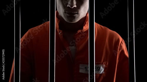 Criminal in orange uniform behind prison bars, serving life sentence for murder