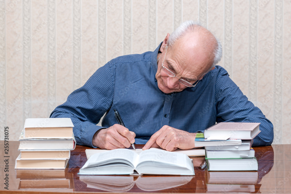old male scientist writes in a notebook, books on the table
