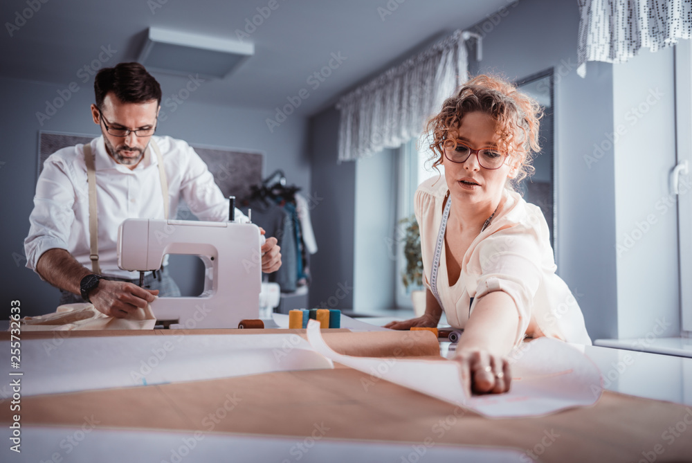 Obraz premium Professional tailors during work on project using sewing machine at fashion design studio
