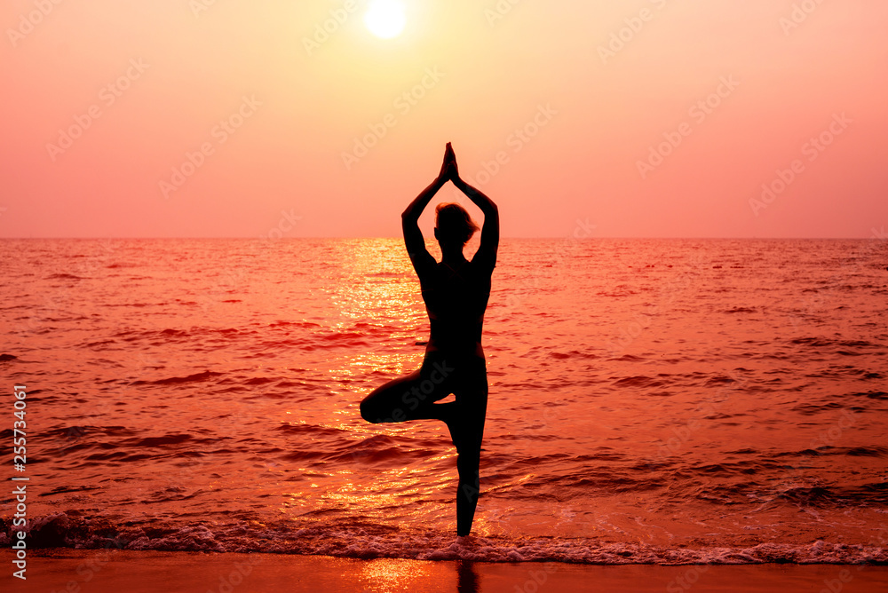 Beautiful young woman practic yoga at the beach. Early morning exercise