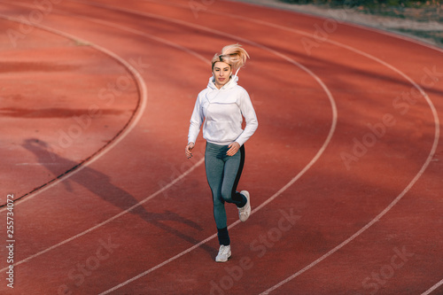 Caucasian female runner in sportswear running on the stadium with earphones in ears. © dusanpetkovic1