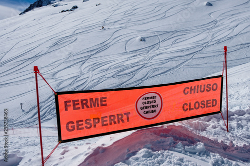 Warning sign in winter, ski slope closed with one skier in background photo