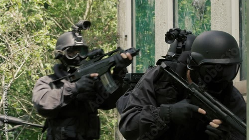 Close Up Four Special Force Soldiers run beside a bedraggled building.