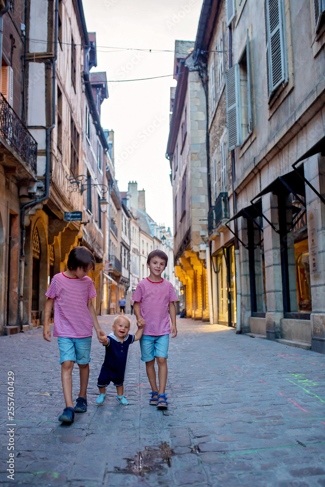 Three children, siblings, boys, walking hand in hands on the street of town of Dijon