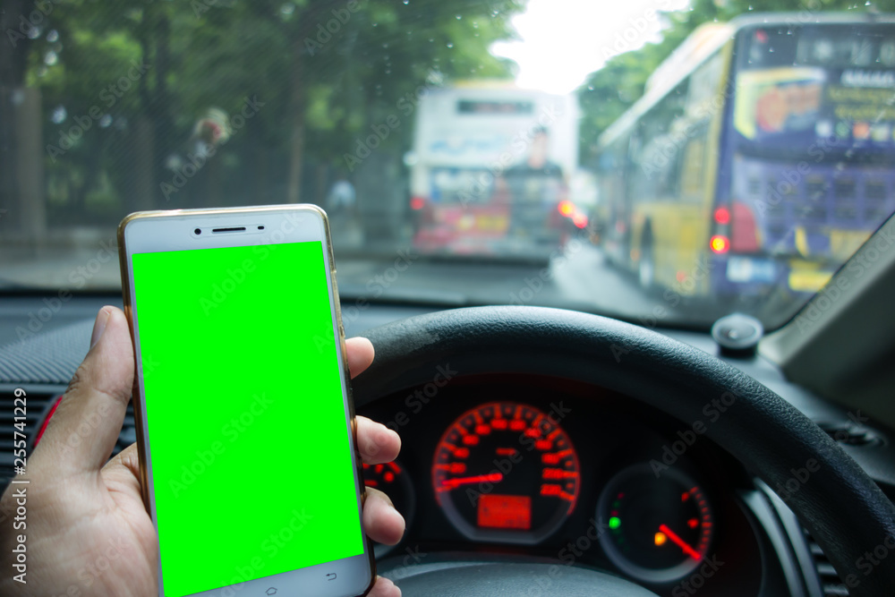 Male driver holding white mobile smart phone on the green screen with blurred traffic jam and empty fuel in background