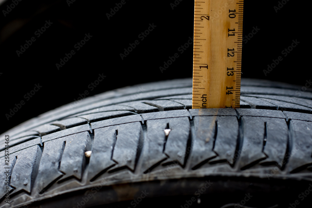 Close up wood ruler measure the tread of black tire Close up wood ruler measure the tread of black tire