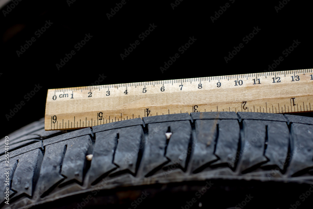 Close up wood ruler measure the tread of black tire Close up wood ruler measure the tread of black tire