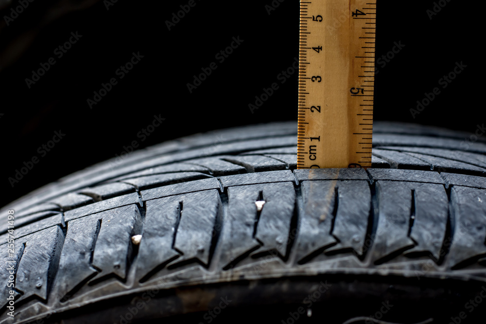 Close up wood ruler measure the tread of black tire Close up wood ruler measure the tread of black tire