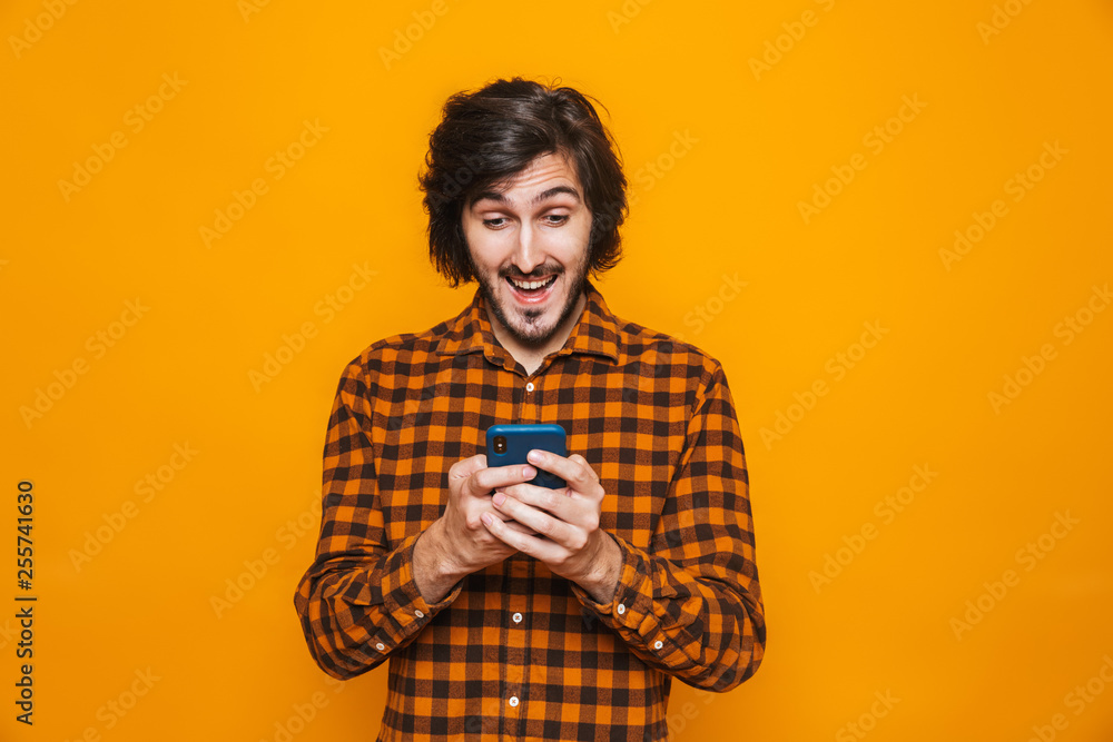 Photo of mustached man wearing plaid shirt laughing and using cell phone while standing isolated Photo of mustached man wearing plaid shirt laughing and using cell phone while standing isolated
