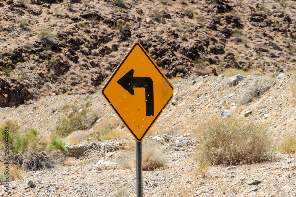 Yellow traffic sign Left Turn in the desert with bullet marks
