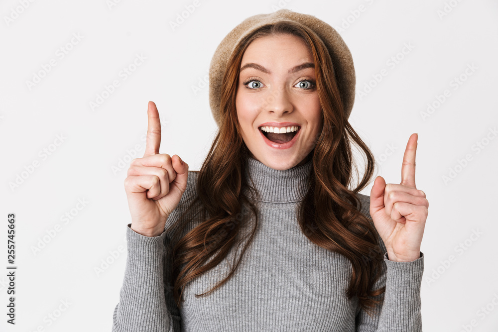 Portrait of caucasian woman 30s wearing hat smiling and pointing fingers upward at copyspace Portrait of caucasian woman 30s wearing hat smiling and pointing fingers upward at copyspace