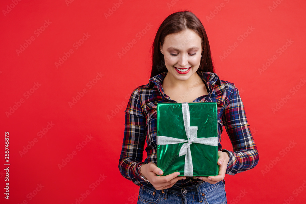 Beautiful girl in plaid shirt holding a box of gifts in an isolated room on a red background Beautiful girl in plaid shirt holding a box of gifts in an isolated room on a red background