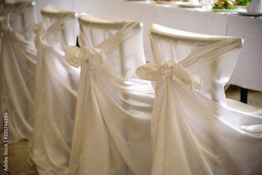 Decorated chairs with black fabric and big pink satin bows. Silk bow tied on back of chair in party at restaurant. Dark cloth cover chairs standing in a row Decorated chairs with black fabric and big pink satin bows. Silk bow tied on back of chair in party at restaurant. Dark cloth cover chairs standing in a row