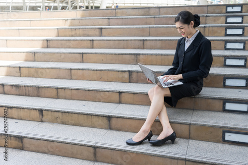 Asian businesswoman smile and sit on the staircase, she typing word into laptop