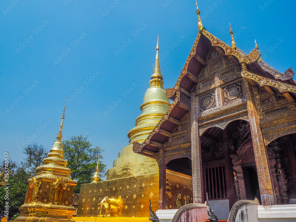 Naklejka premium Ancient wooden temple and gold pagoda with blue sky background