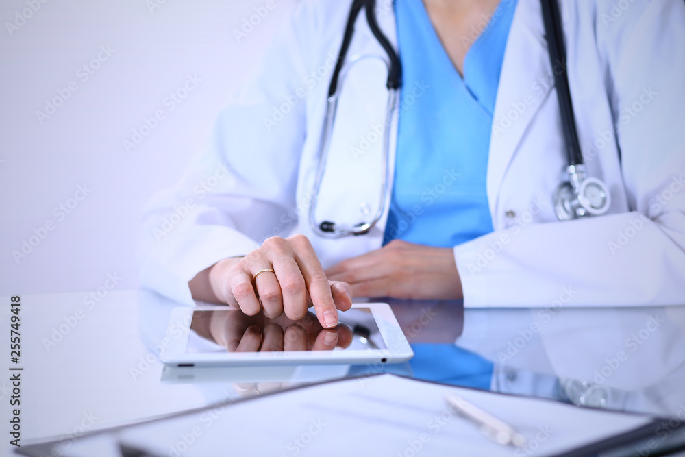 Woman doctor using tablet computer while standing straight in hospital office, closeup. Healthcare, insurance and medicine concept