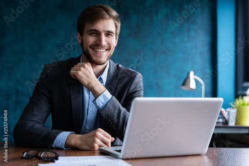 Happy young businessman using laptop at his office desk.