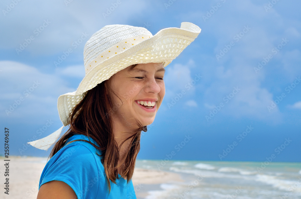 Young girl in a white hat on the sea beach. Clean, sandy beach against the blue sea.