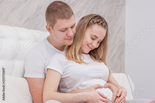 Smiling pregnant woman and her husband hugging on the bed