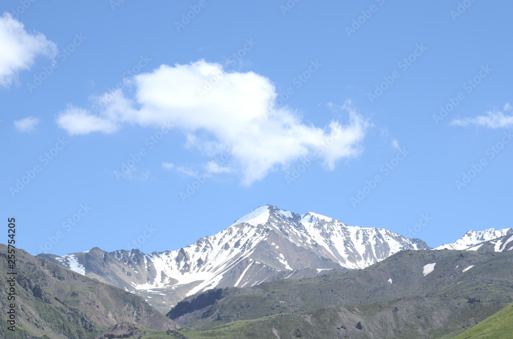 Mountains with peaks covered with snow, white clouds on blue sky,  Caucasus