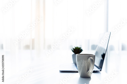 Business workspace with laptop on white table in the morning sun light, Coffee cup in the working time © NARANAT STUDIO