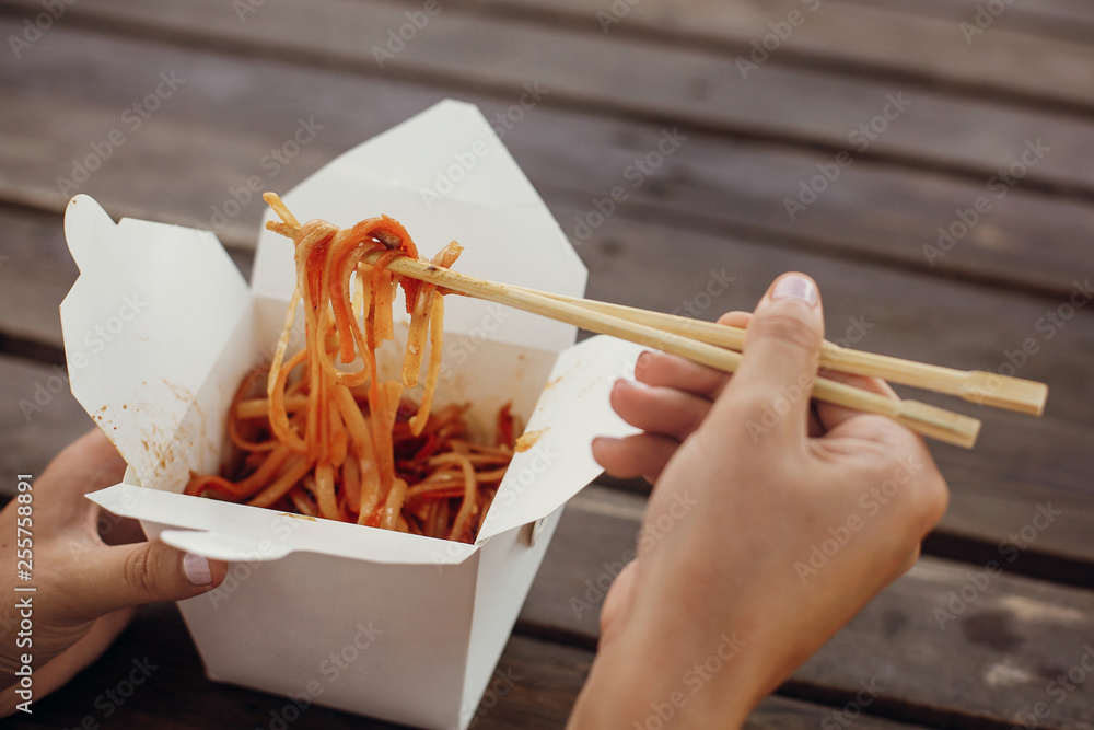 Wok with noodles and vegetables in carton box to go and bamboo chopsticks.  Traditional Asian cuisine. Asian Street food festival. Girl eating thai  noodles in open box takeaway. Food delivery foto de