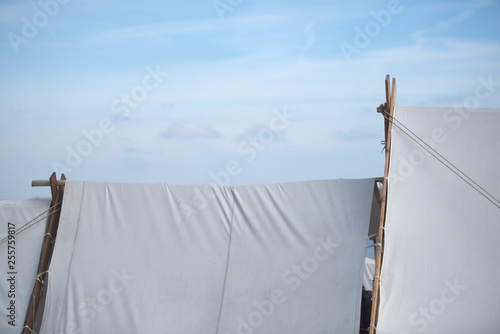 White cloth tent, tipi with wooden poles and blue sky with white clouds