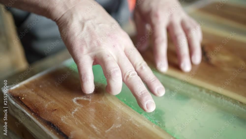 Tracking close-up of unrecognizable mature furniture maker creating epoxy resin decoration on unfinished wooden tabletop placed on workbench Tracking close-up of unrecognizable mature furniture maker creating epoxy resin decoration on unfinished wooden tabletop placed on workbench