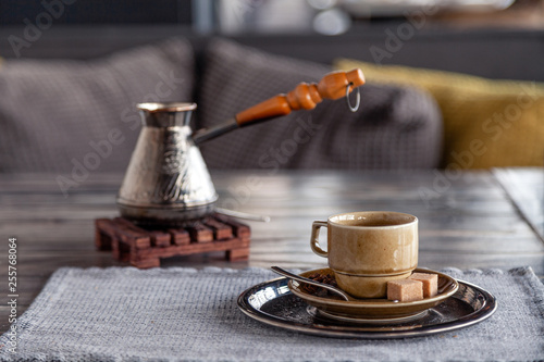 Closeup traditional Turkish coffee in cezve on wooden stand, porcelain cup with refined sugar cubes served on table in restaurant. Сoncept breakfast in restaurant at luxury hotel photo