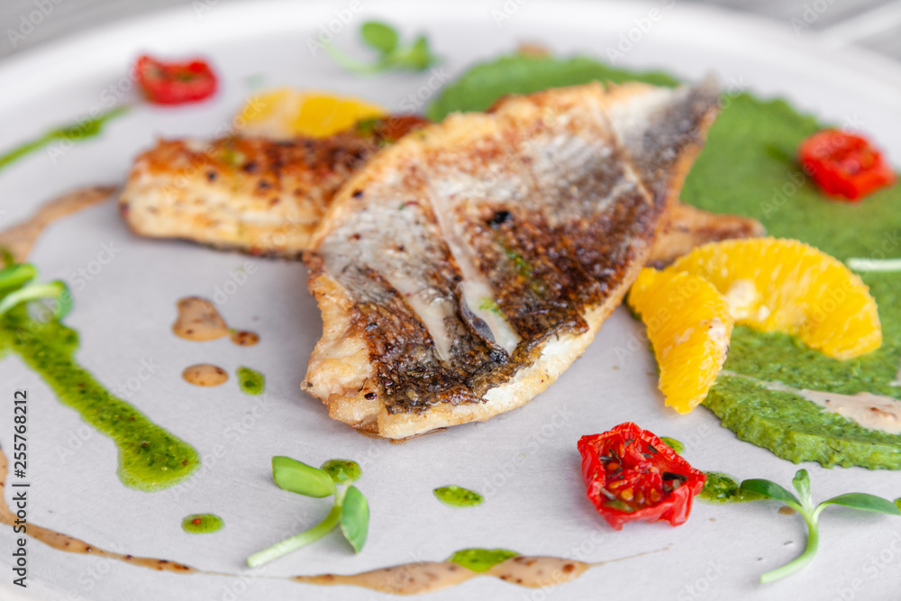 Closeup fried sea bass fillet with green pea puree, tomatoes, sauce, orange slices. Concept professional photography, photosession new menu, profession food stylist, flat-lay, freelancer